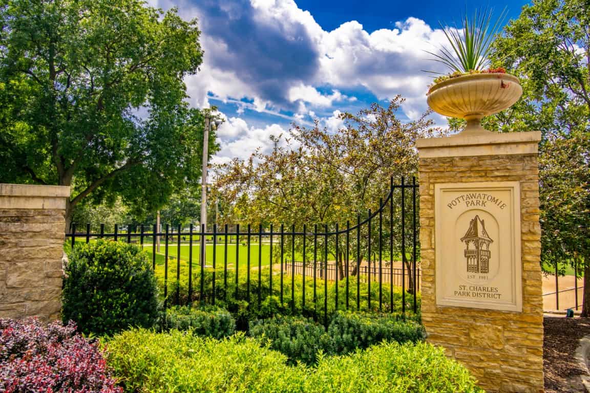 Entrance to Pottawatomie Park in St Charles Illinois with stone pillars, iron fence, and landscaped gardens